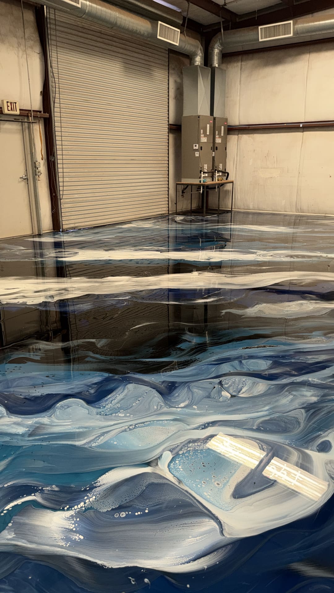 Blue and white metallic epoxy swirling across a shop floor in front of a roll up door