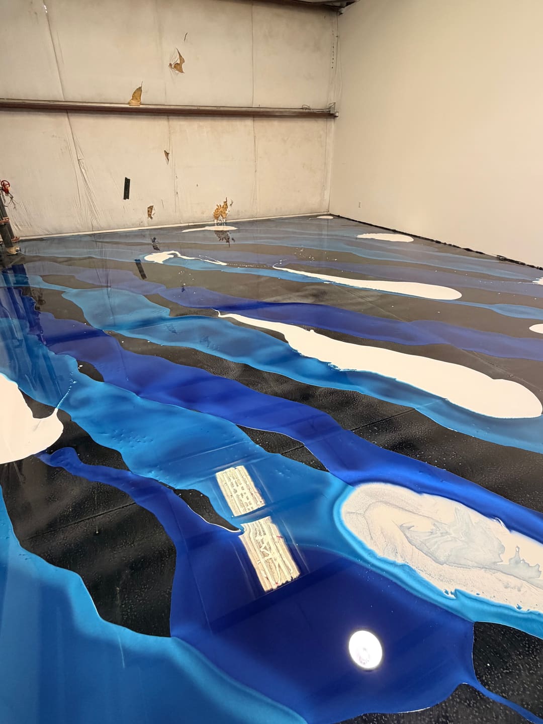 A finished blue, black and white metallic epoxy floor across an empty warehouse, still wet looking under the shop lights