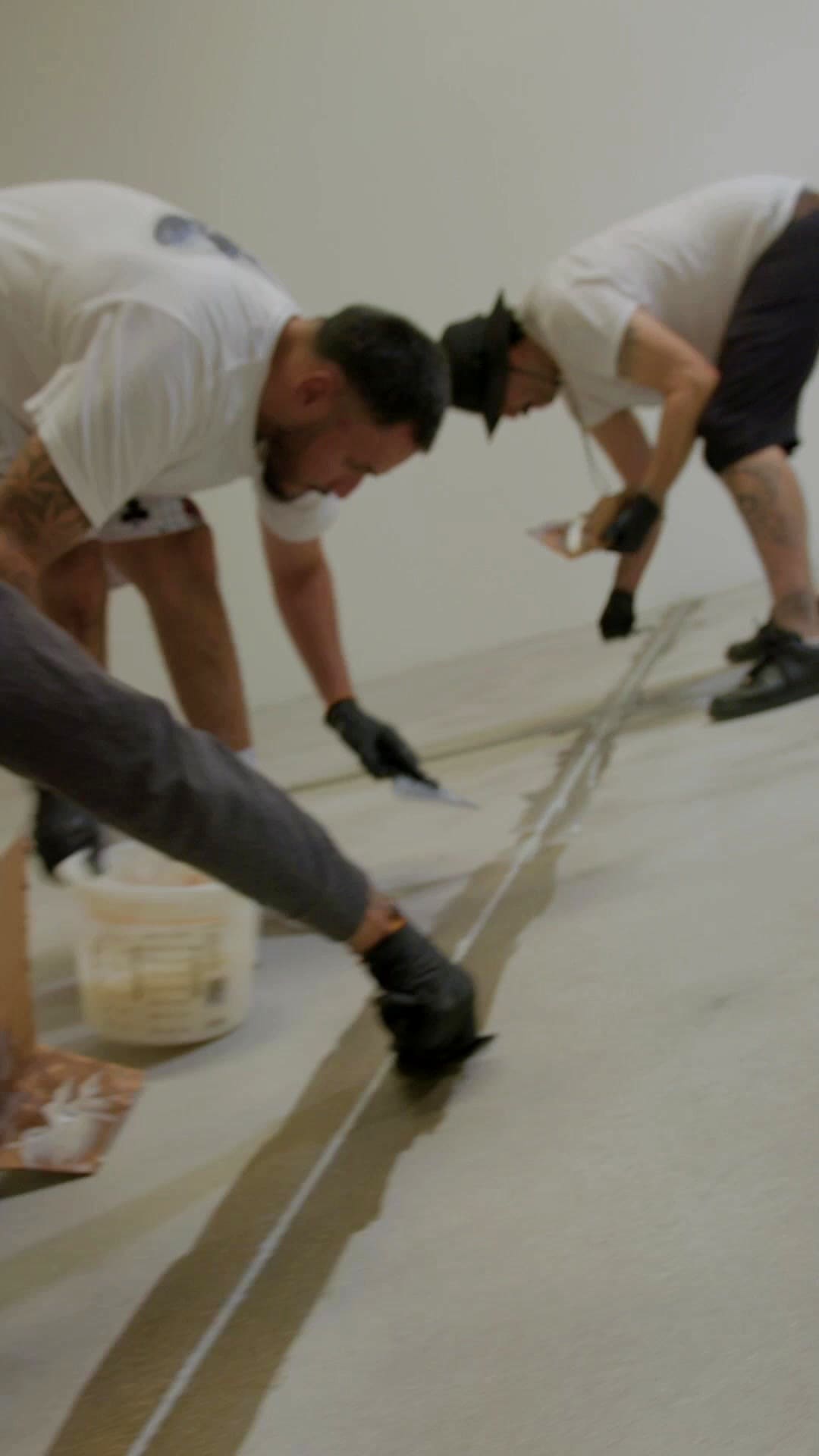Two of the crew on their knees filling the joints in a bare concrete slab before the coating goes down