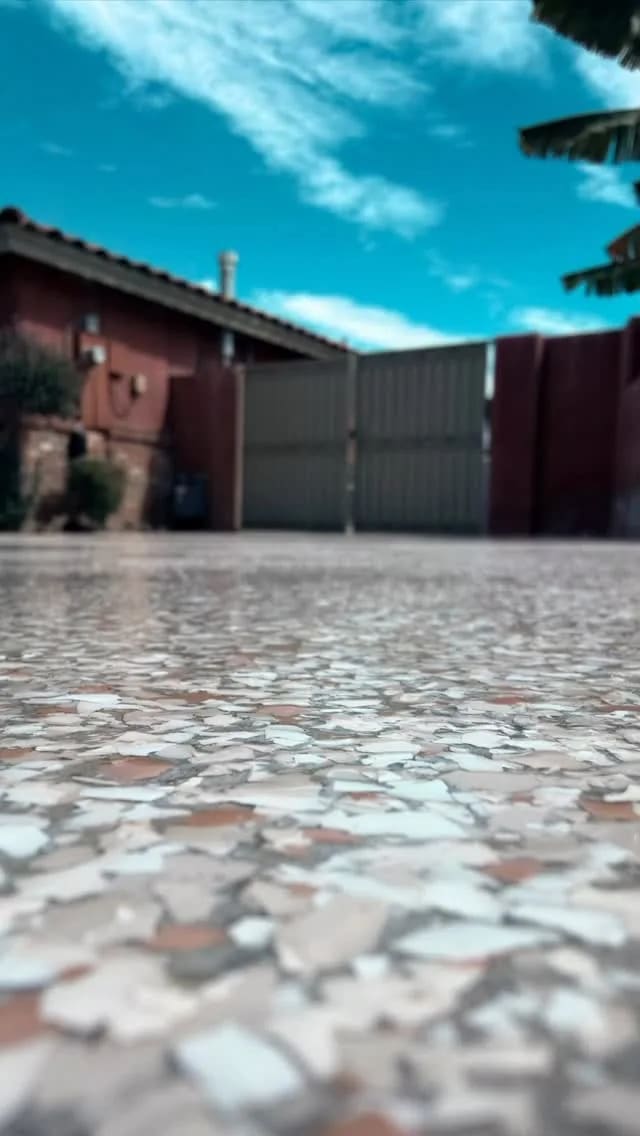 A cream, grey and rust flake epoxy patio running up to a metal side gate under a blue sky