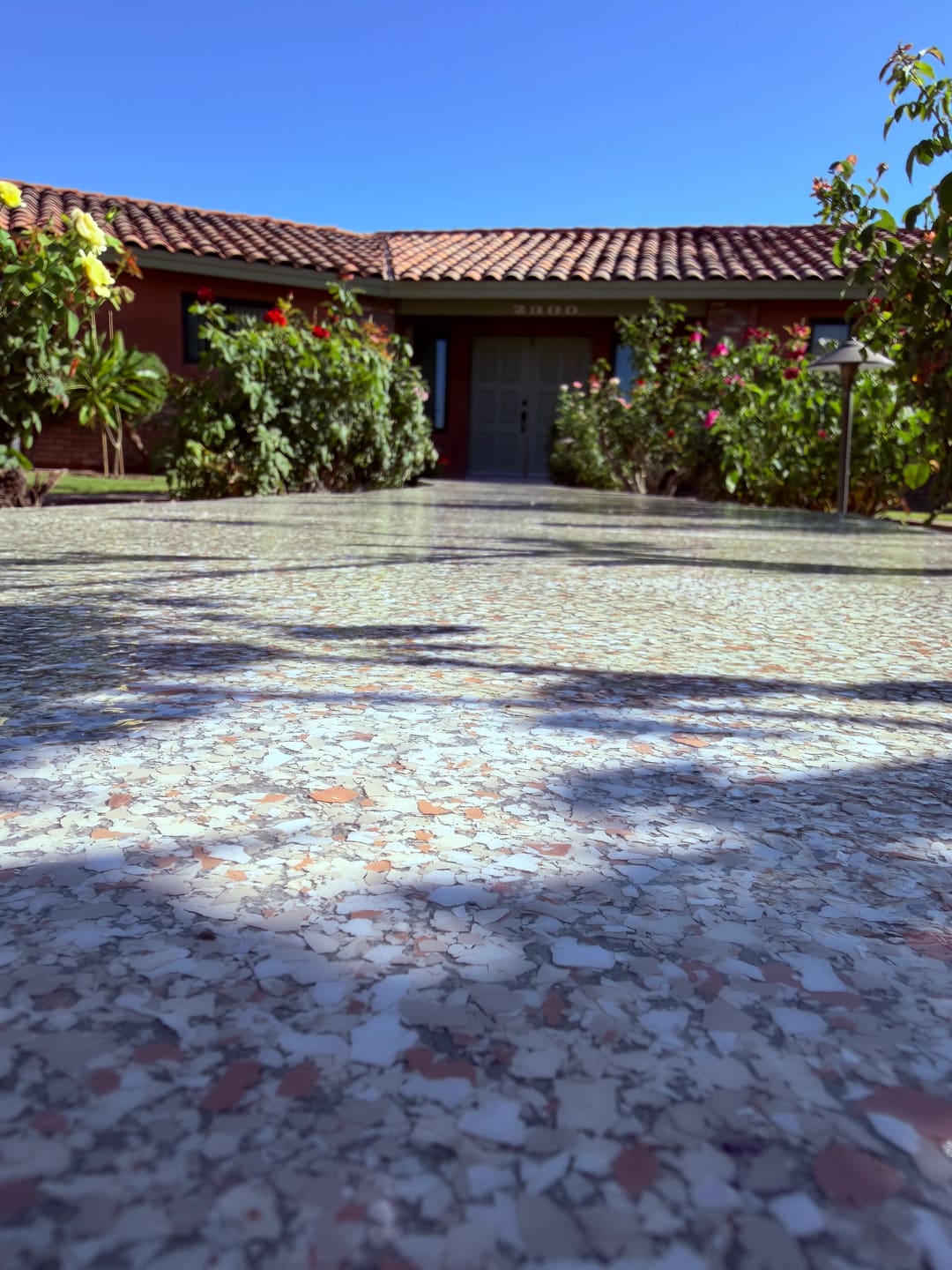 A grey and white flake epoxy driveway leading up to a red tile roof house with rose bushes