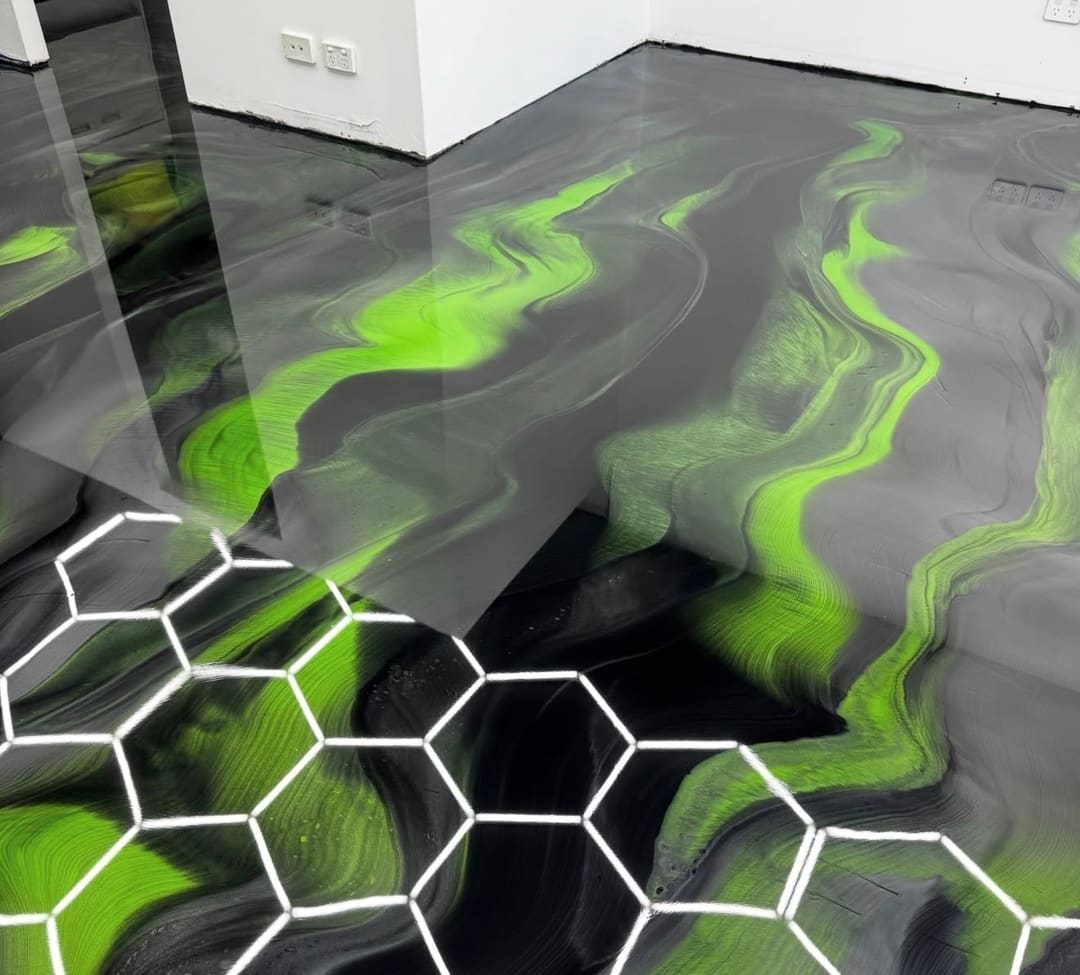A grey and black metallic epoxy floor with neon green veins, reflecting a hexagon light grid in the ceiling